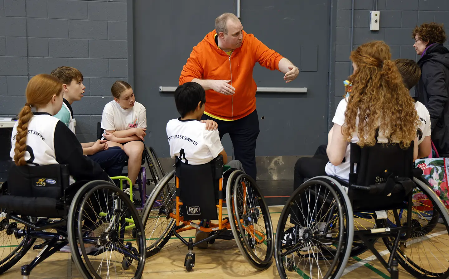 wheelchair basketball coach talking to a group of junior wheelchair basketball players
